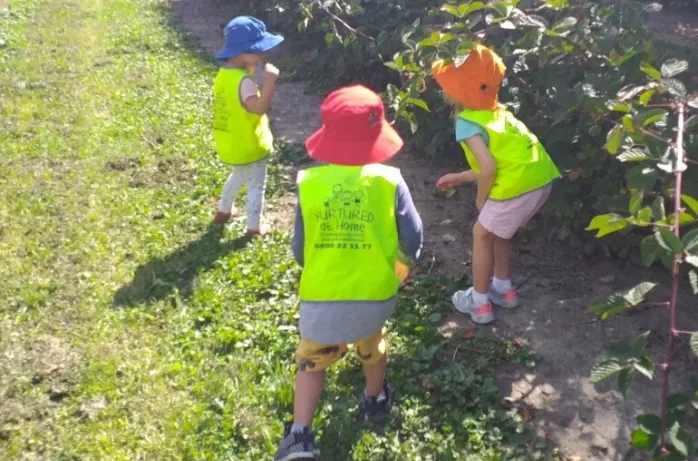 Three young children in hi-vis vests and sunhats explore a garden path.