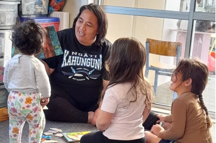 An educator shows a picture book to a group of young children sitting on the floor.