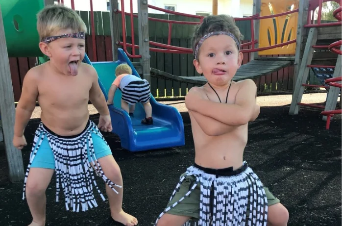 Two young boys in piupiu pulling pūkana faces in a playground.