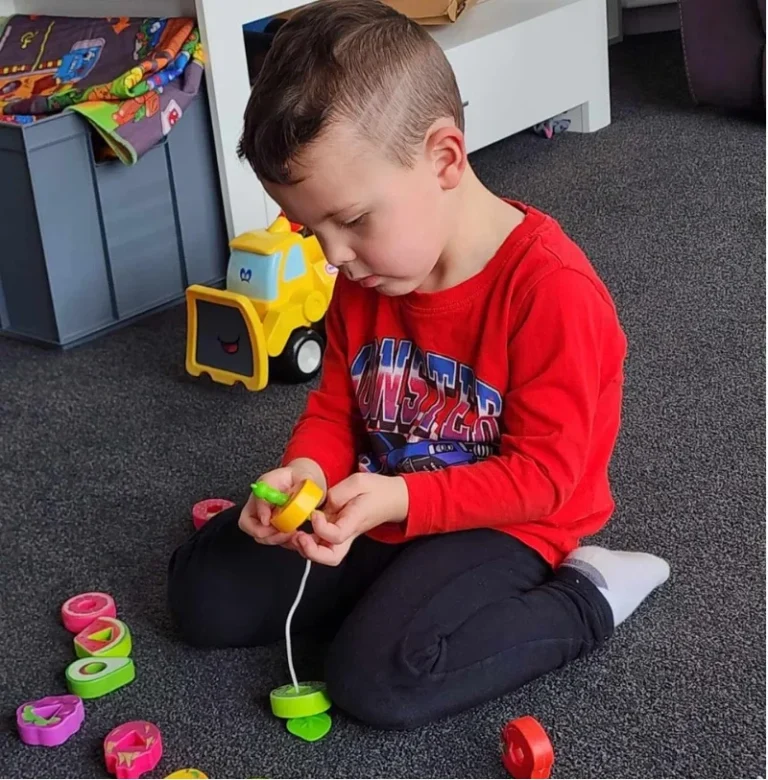 A boy threads large coloured beads onto a string.