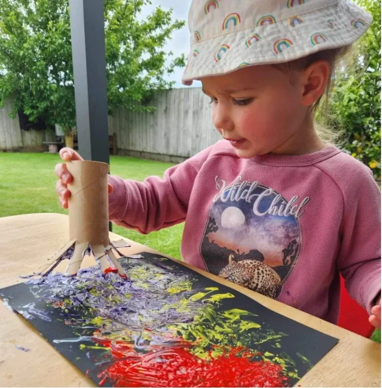 A toddler paints on black paper with a cardboard-tube brush outdoors.