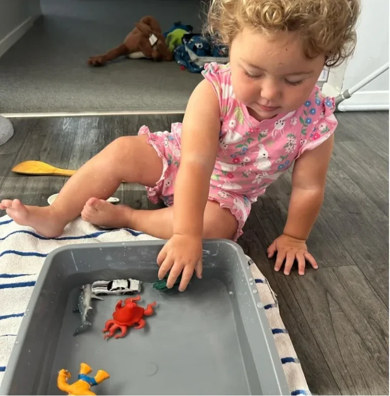 A toddler plays with toy sea creatures in a tray of water.