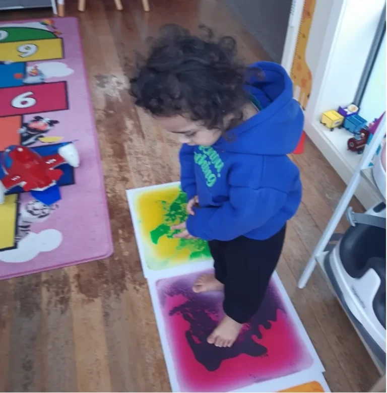 A toddler stands on colourful sensory floor tiles.