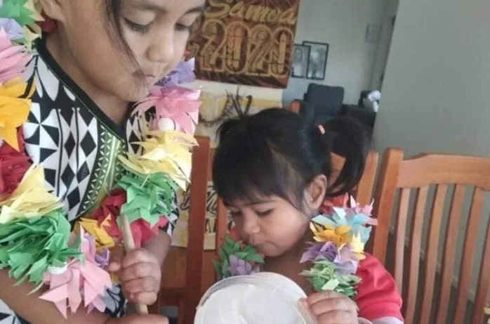 Two young children wearing colourful paper flower lei.