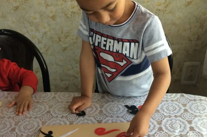 A boy arranges cut-out shapes on a table.