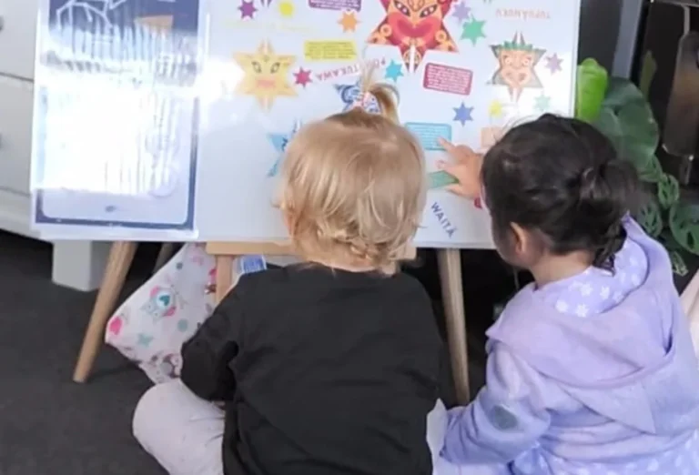 Two toddlers look at a Matariki star display on an easel.
