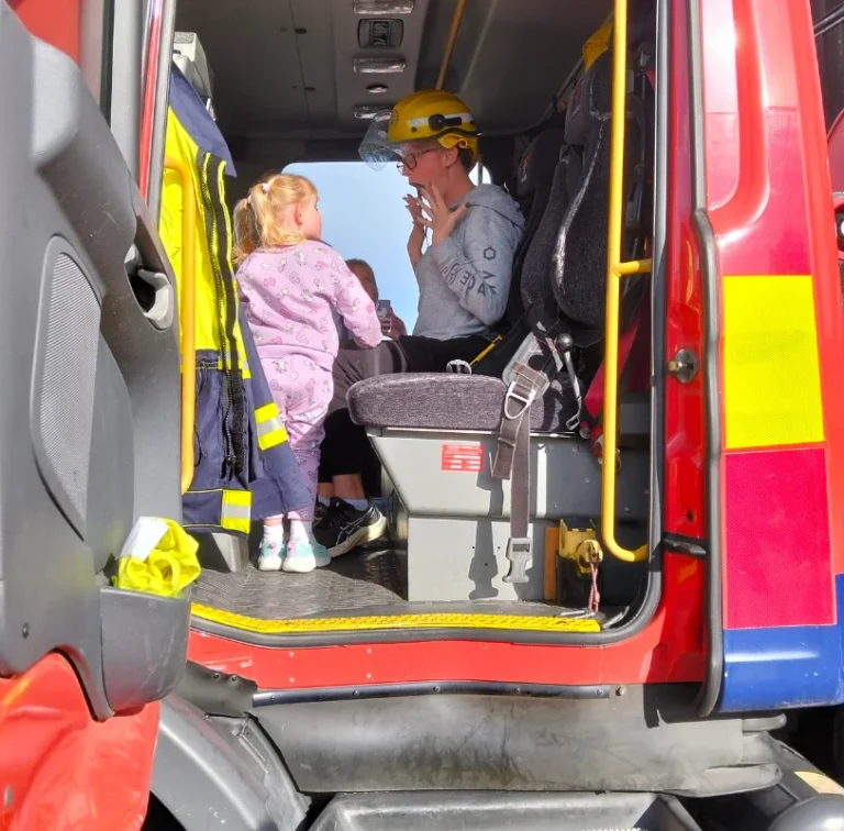 A child looks into the cab of a fire engine while a firefighter sits inside.
