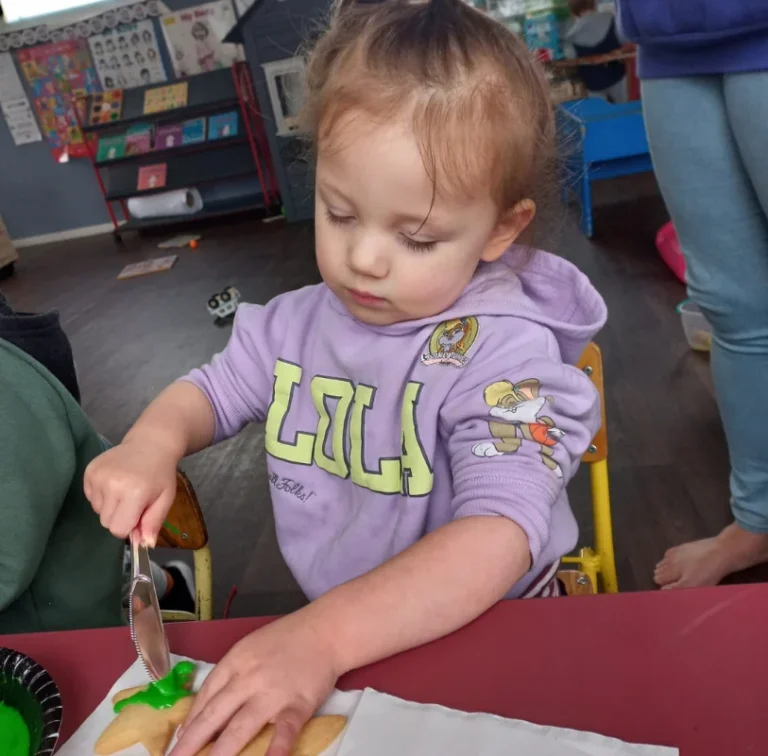 A toddler cuts dough with a pizza cutter at a table.