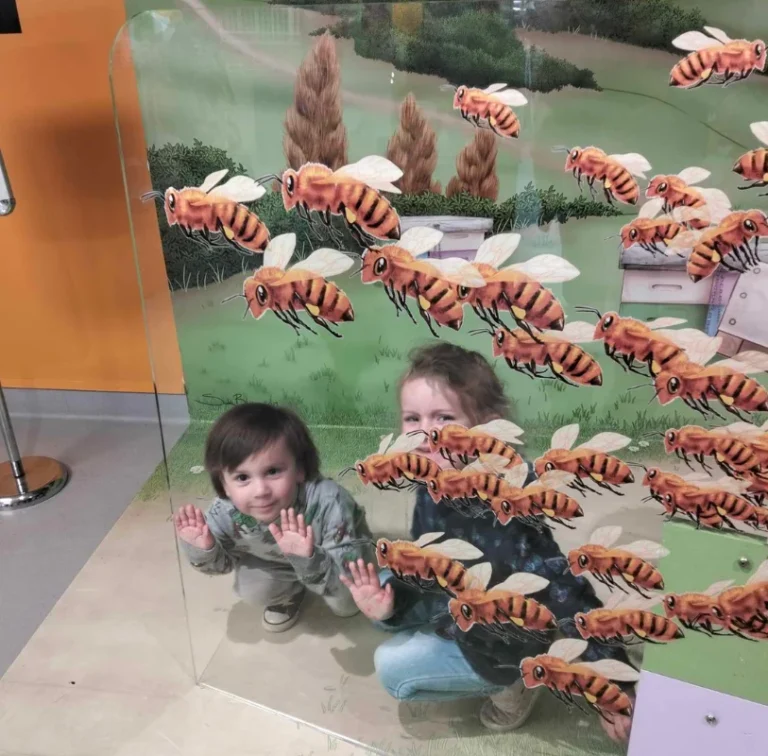 A toddler and an adult press their hands against a glass display of giant bees.