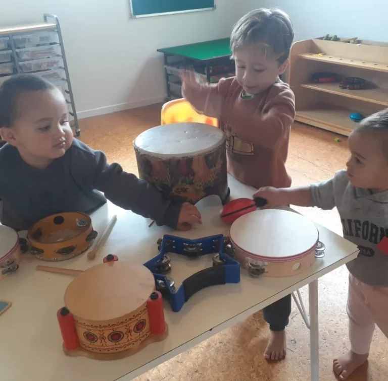Young children play drums and tambourines at a table.