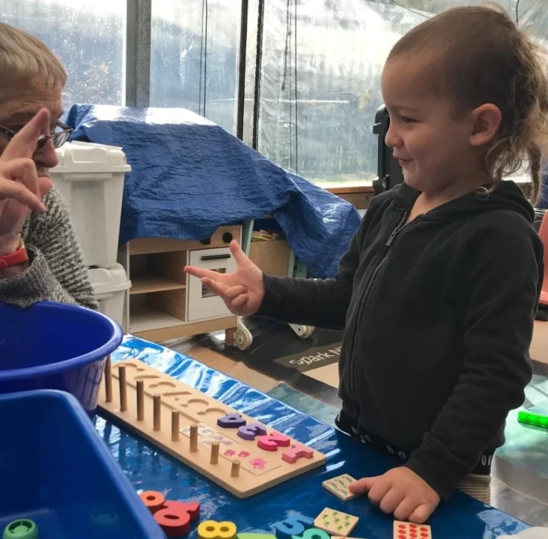 A child counts on her fingers beside a number peg board.