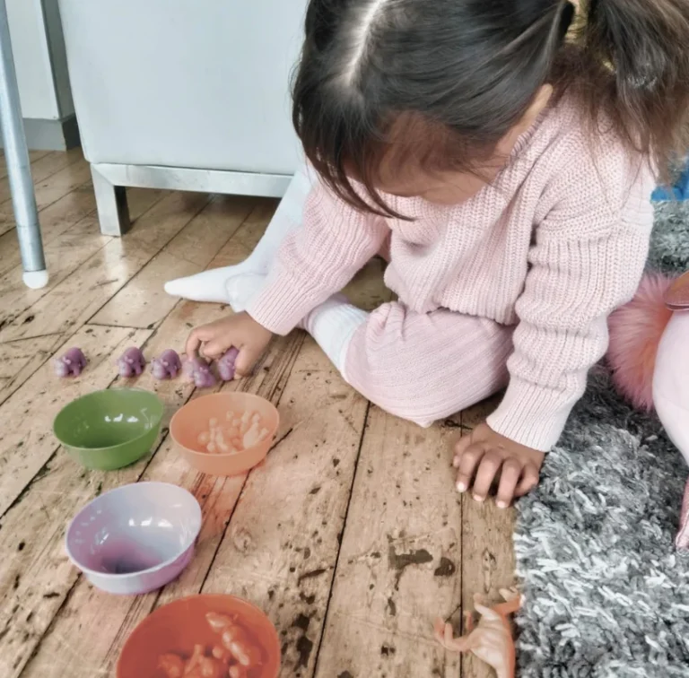 A girl sorts play dough into coloured bowls on the floor.