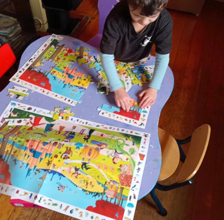 A boy works on a large jigsaw puzzle at a table.