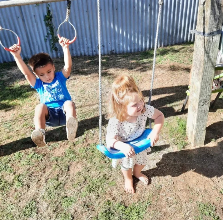 Two young children play on swings in a backyard.