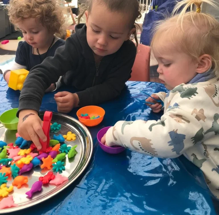 Young children use tweezers to sort colourful counters into bowls.