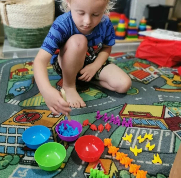A boy sorts coloured counting bears into bowls on a road play mat.