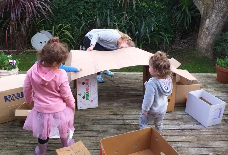 Young children play with large cardboard boxes on a deck.