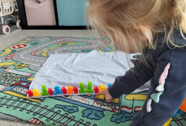 A toddler lines up coloured counting bears in a row on a road play mat.
