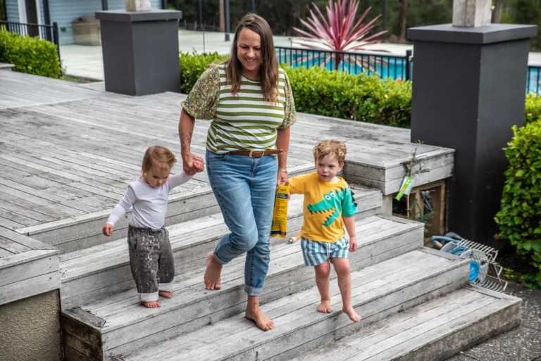 An educator walks hand in hand with two toddlers down wooden deck steps.