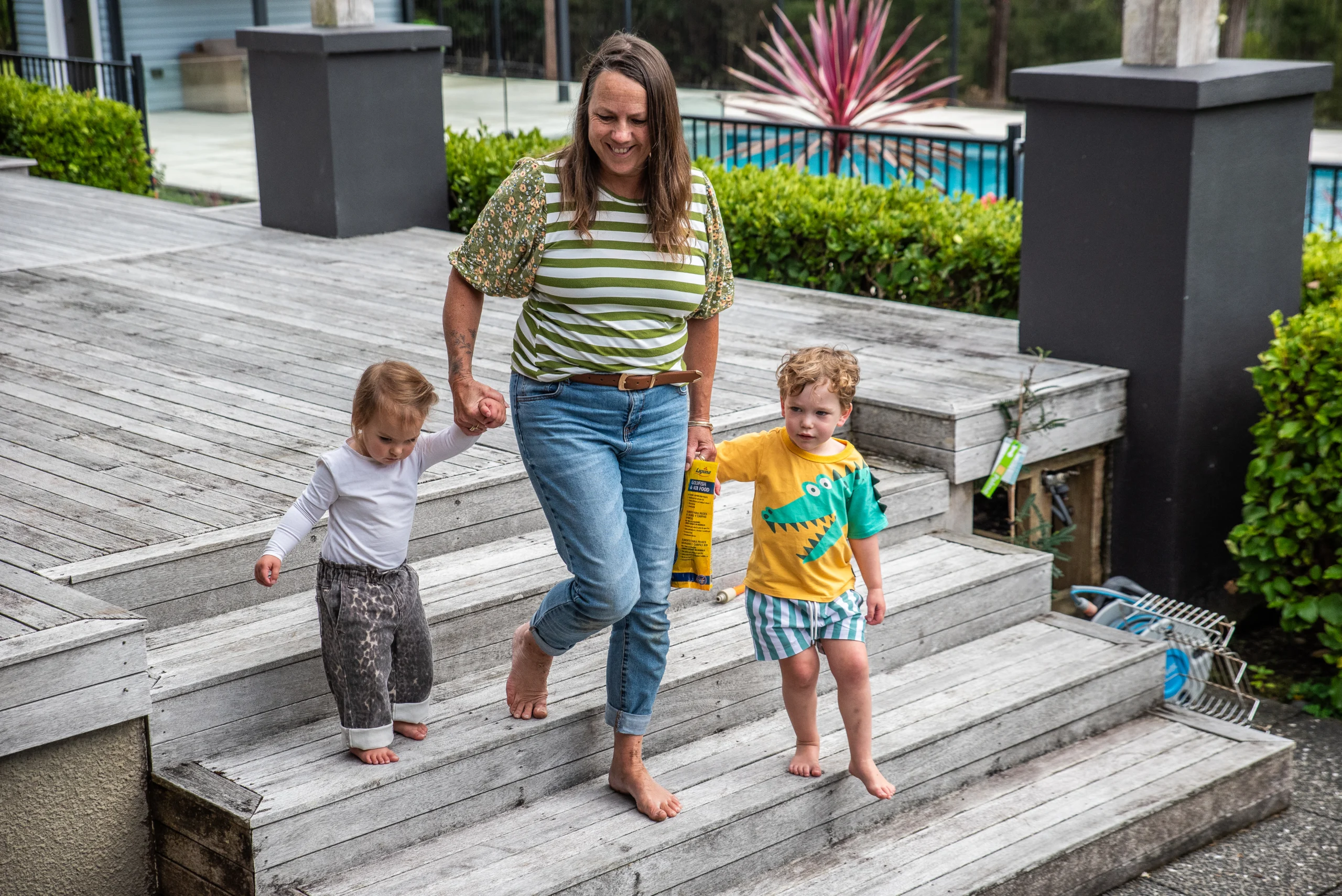 An educator walks hand in hand with two toddlers down wooden deck steps.
