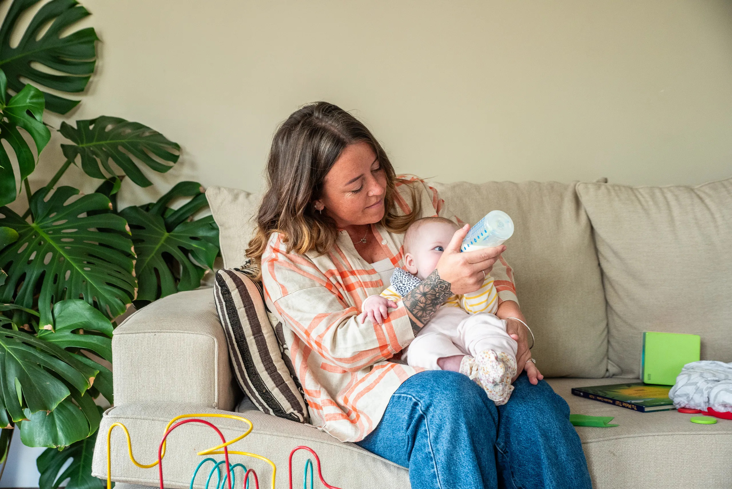 An Educator feeding a baby a bottle on a couch in a bright living room
