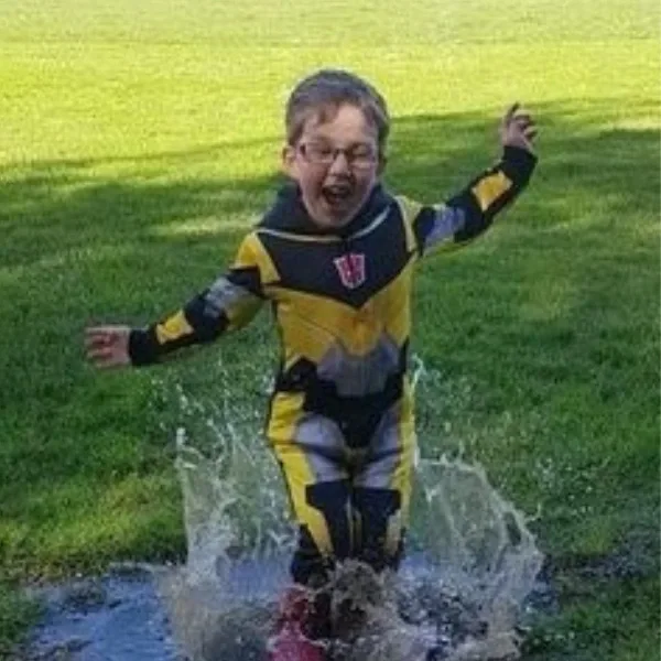 A child in a rain suit jumping in a puddle, in Donna's care in Totara Park