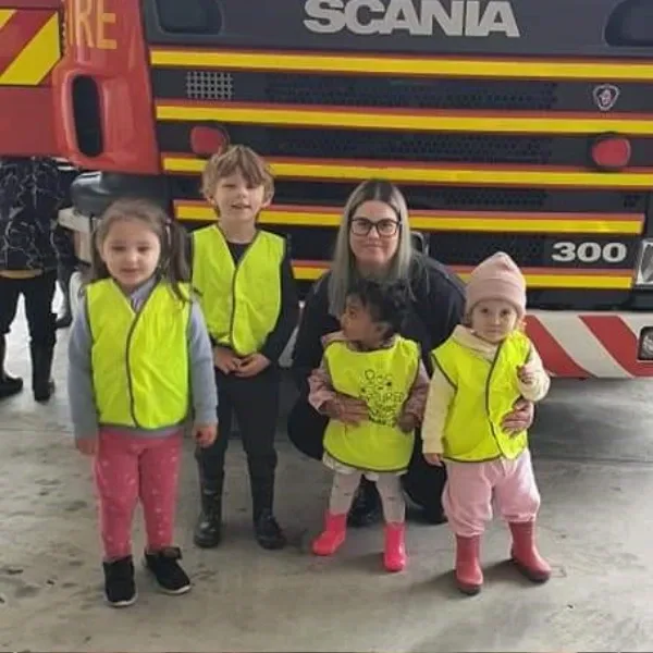 Children in hi-vis vests beside a fire engine on an outing with Kirsty, home-based educator in Maoribank