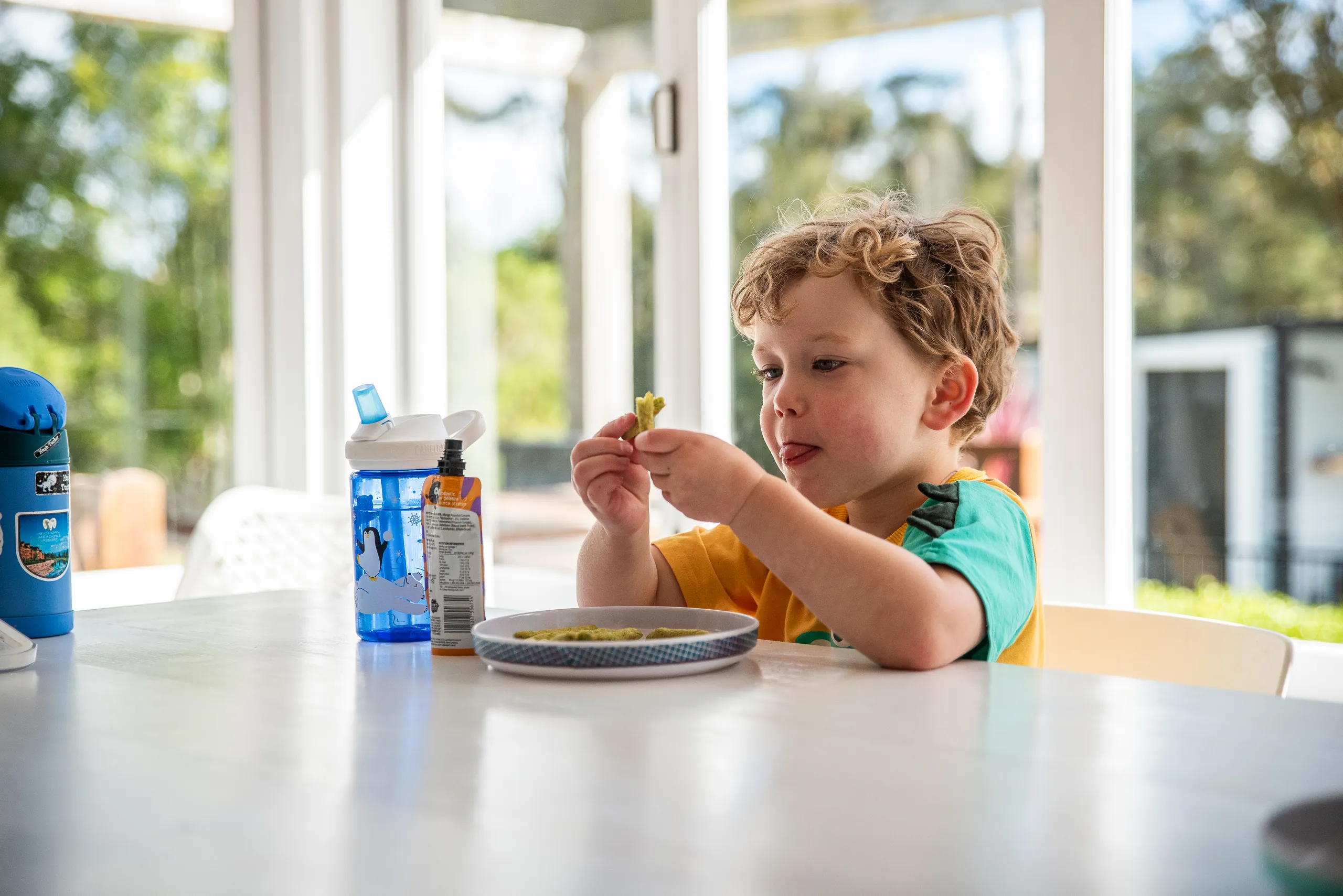 A young boy eating a snack at a table in a sunny room